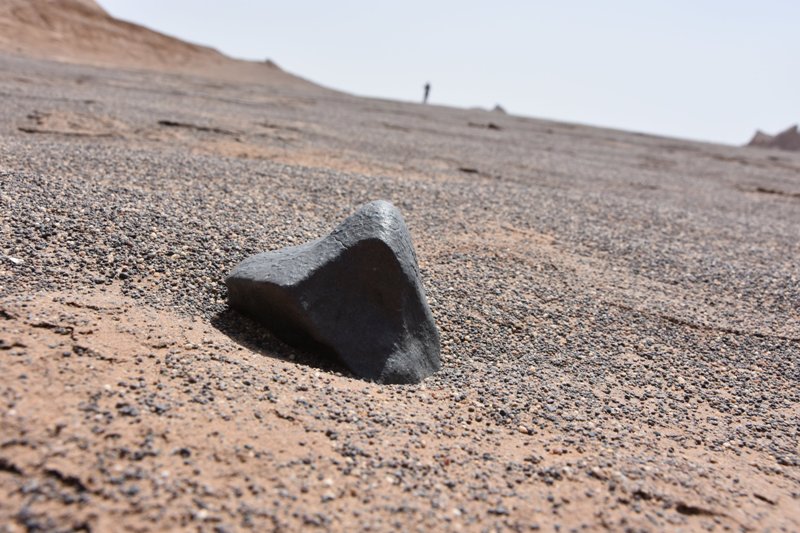 Uno degli esemplari più grandi rinvenuti: è una condrite di quasi un chilo  che presenta spaccature ed una bella crosta di fusione; sullo sfondo i Kalut